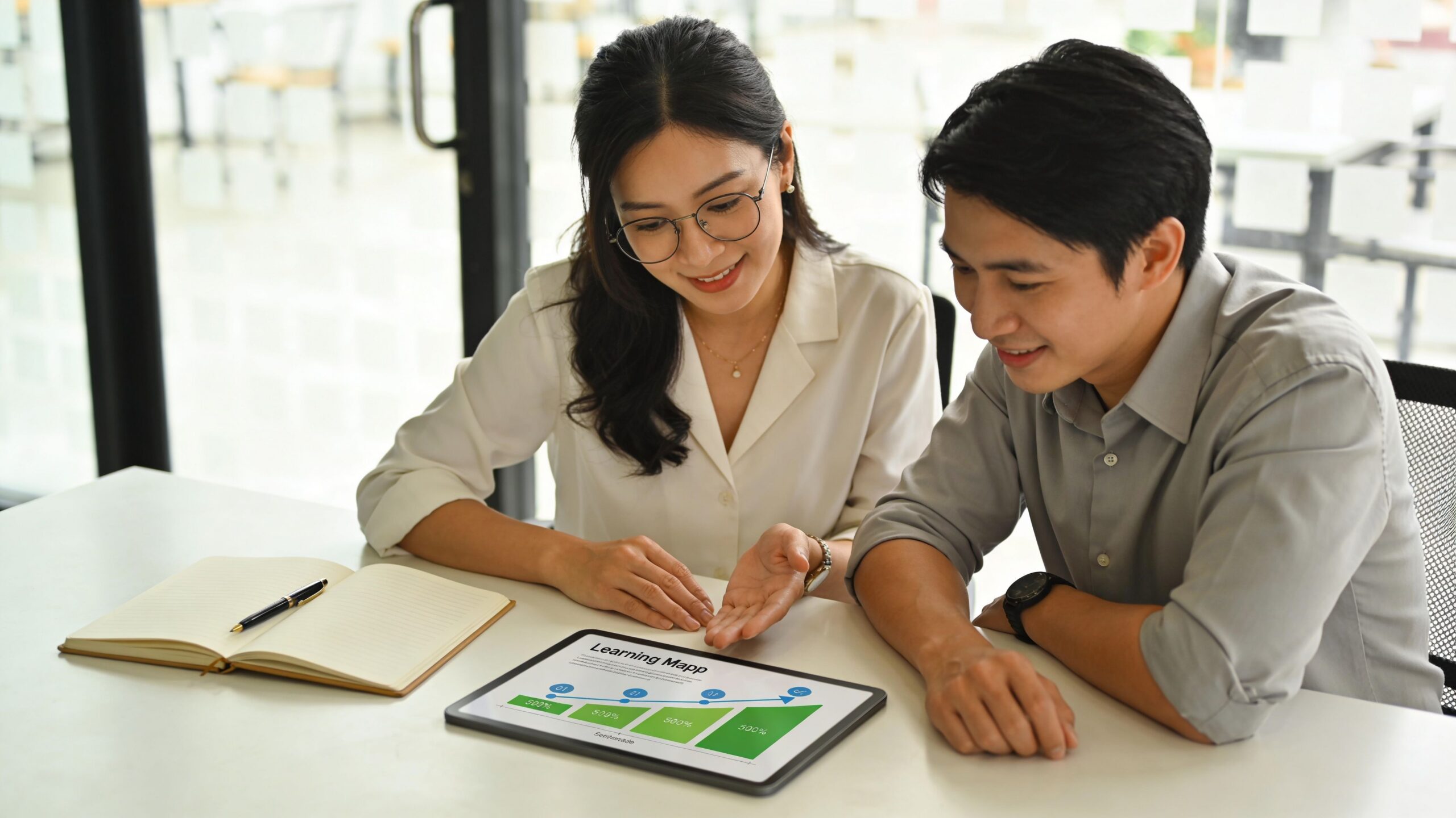 Deux collègues professionnels analysent un graphique de progression sur une tablette numérique dans un bureau moderne.